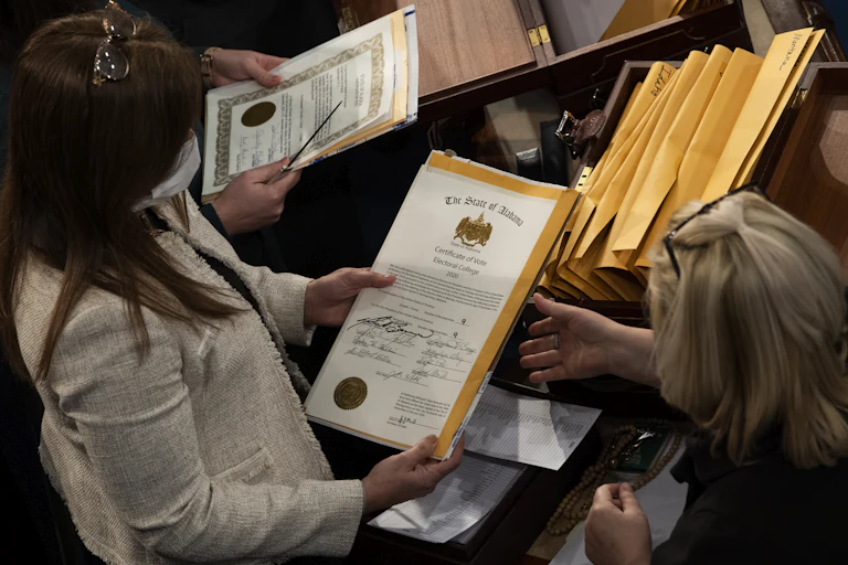 Two women hold documents with seals for the state of Alabama with the wording, “Certificate of Vote, Electoral College, 2020.”