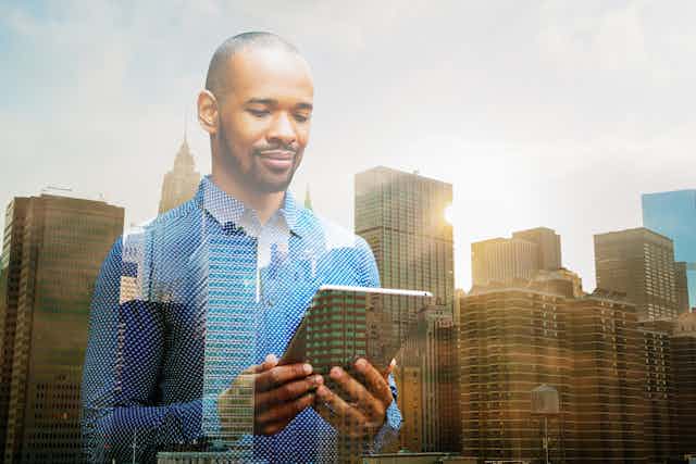 The image of a Black man looking at an iPad is fused with a backdrop of skyscrapers.