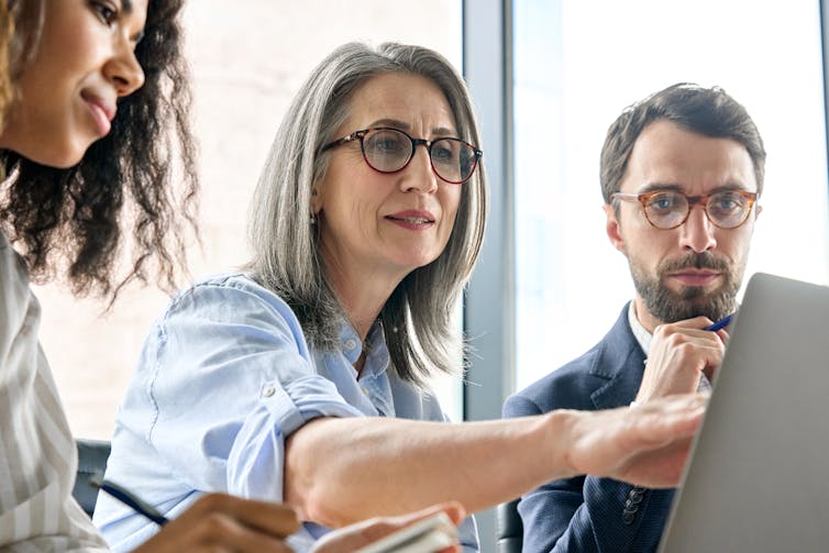 Two women and man looking at computer screen in office, one woman pointing to screen