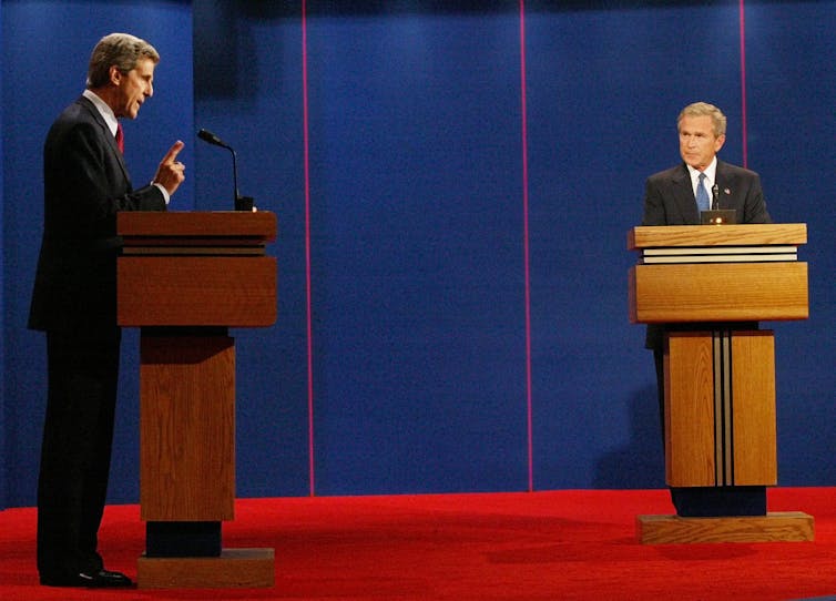 Two men in dark suits debating each other from different lecterns.