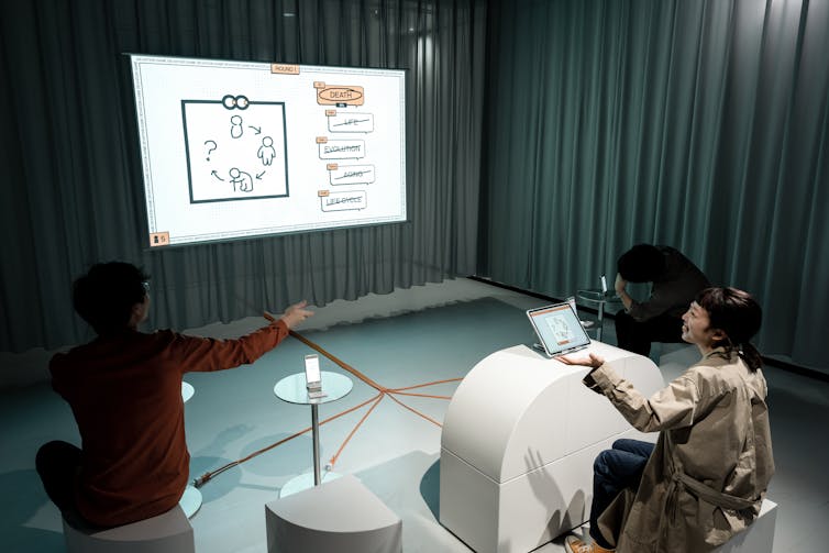 trois personnes sont assises autour d’un écran, l’une d’entre elles dessine sur une tablette