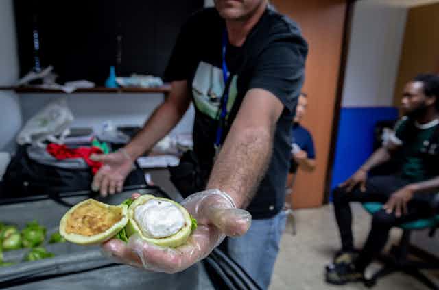 Un homme montre un fruit ouvert en deux, dans lequel a été dissimulé un gros sachet de cocaïne