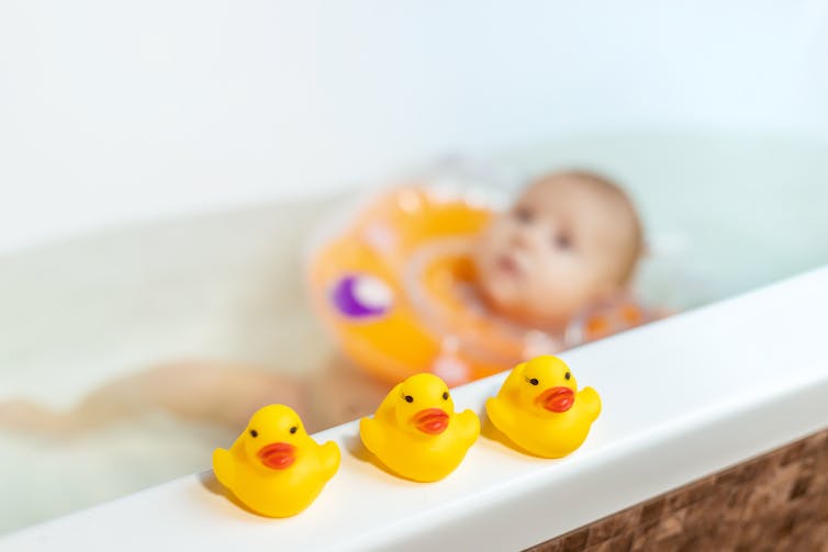 baby floating in bath beside rubber ducks