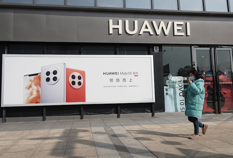 Pedestrian walks past a Huawei store and billboard