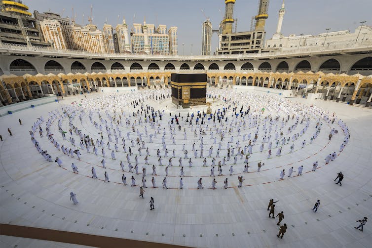 People walk around a black cubic structure along circular rows.