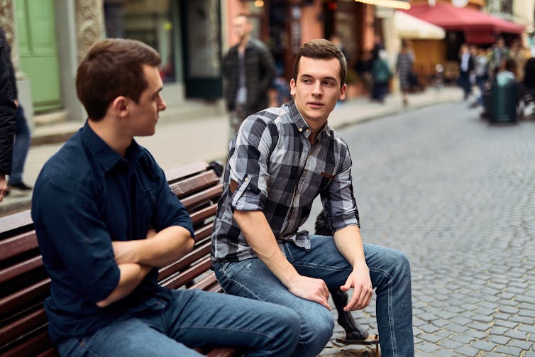 Two young men talking on a bench.
