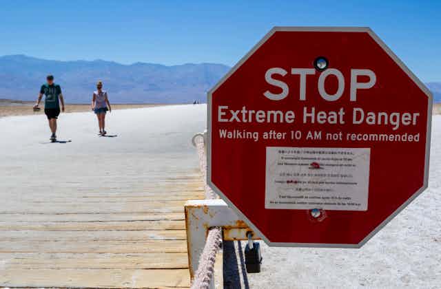 Two people walking on a boardwalk next to a heat warning sign