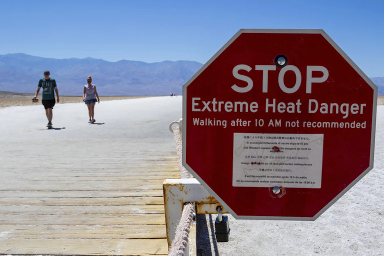 Two people walking on a boardwalk next to a heat warning sign