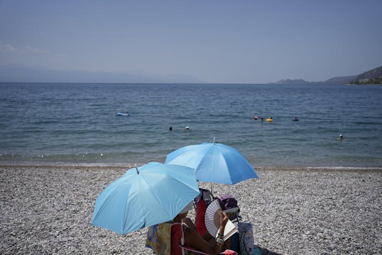 A couple, shaded by umbrellas, on a beach in Greece.