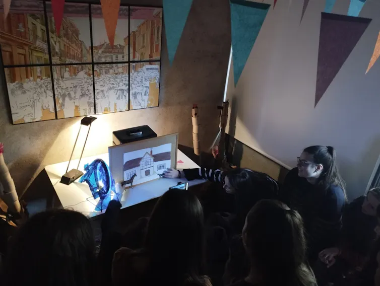 Un grupo de estudiantes a oscuras observa y graba una escena con un dibujo de fondo.
