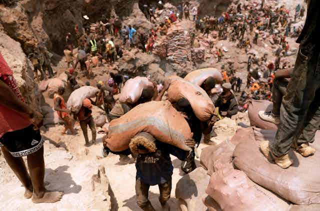 hundreds of people work in a dustry mine, some carrying large sacks of ore on their backs up a hill