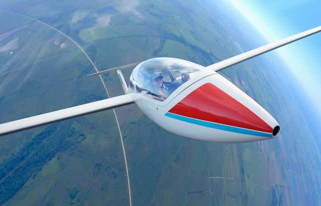 a glider piloted by a woman soars high above a landscape of farm fields