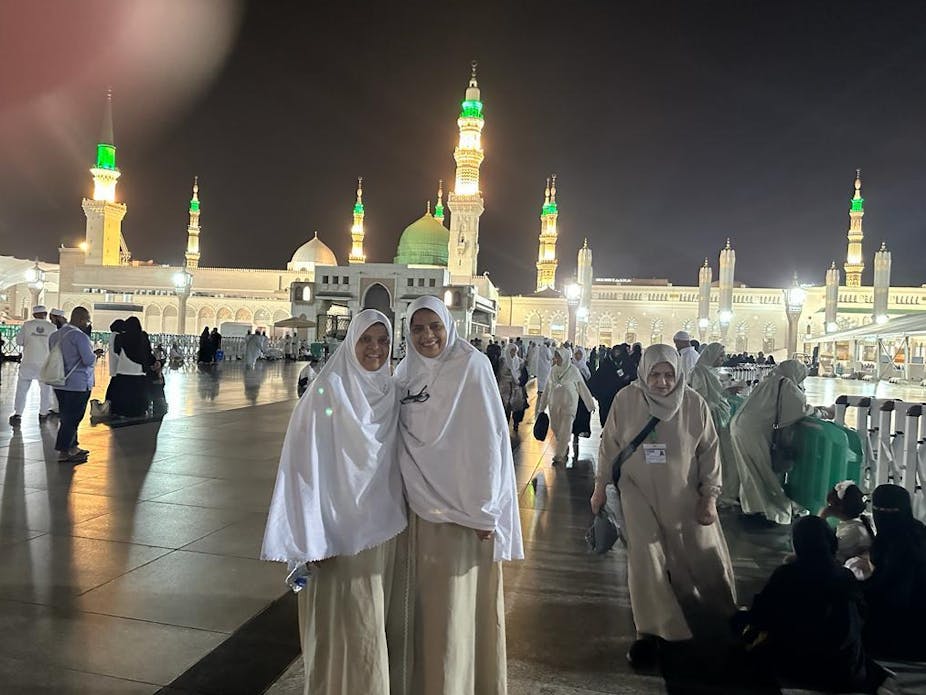 Two women in white headdress pose for an image outside the mosque during hajj.