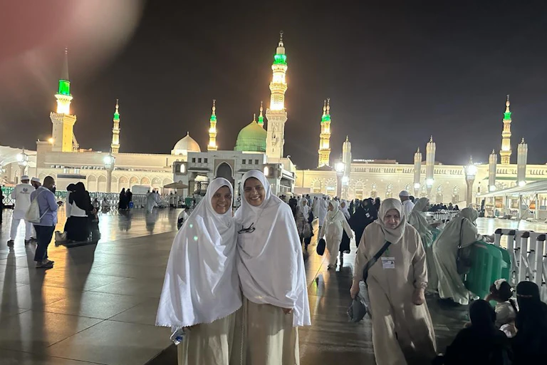Two women in white headdress pose for an image outside the mosque during hajj.