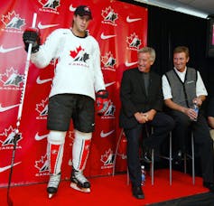A man wears a hockey uniform in front of a red wall blazoned with Nike and Hockey Canada logos