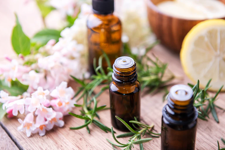 Amidst an array of herbs, fruit and flowers, we see three small dark bottles filled with liquid on a wooden table.