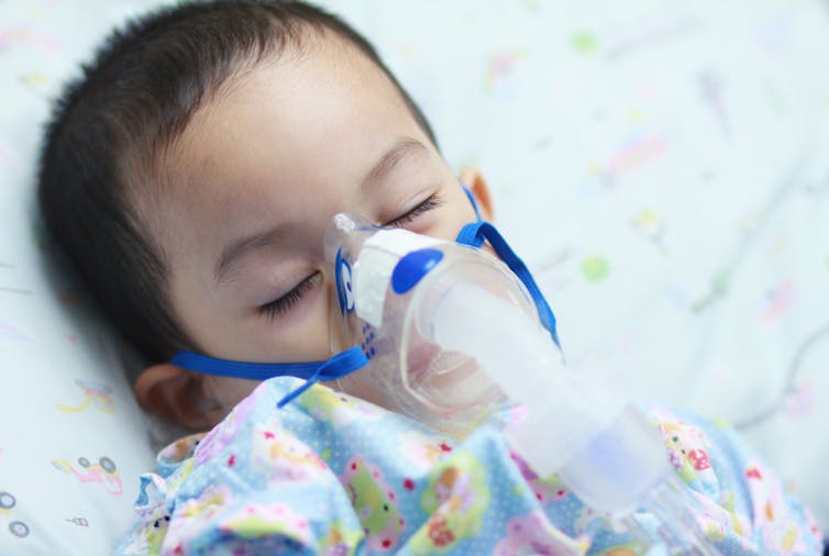 Male toddler with oxygen mask over face in hospital bed