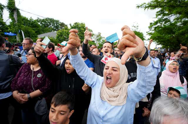 A woman in a hijab makes a thumbs down sign at a protest.
