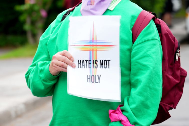 A person in a green shirt holds a paper that reads: hate is not holy.