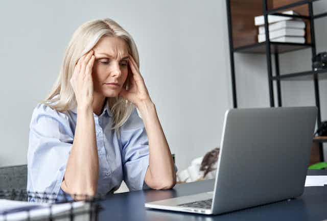 Woman with hands to head, looking distressed, in front of laptop.