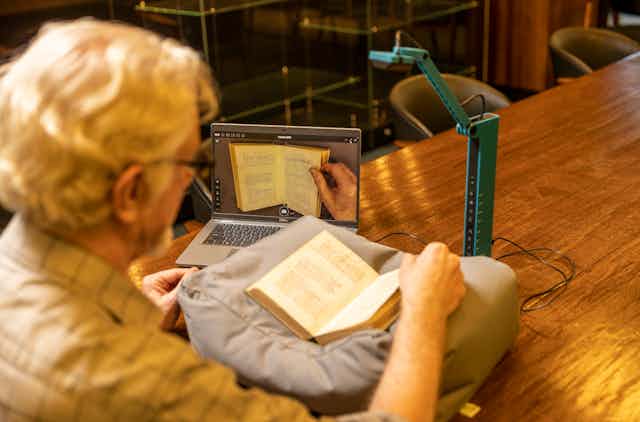 Un hombre abre un libro ante un ordenador y un escáner que lo digitaliza.