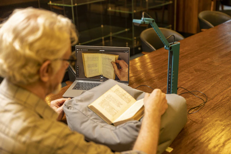 Un hombre abre un libro ante un ordenador y un escáner que lo digitaliza.