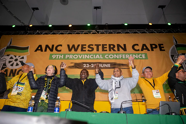 A woman and five mean hold hands aloft.