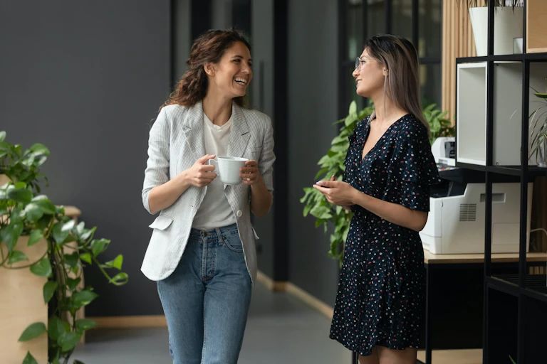 Deux femmes en tenue de travail discutent dans un bureau. en prenant un café
