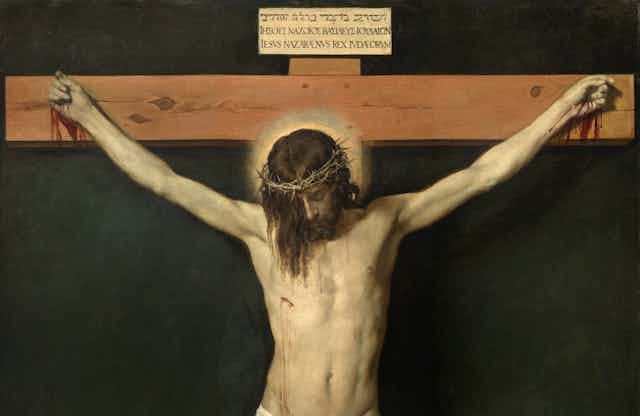 Un hombre medio desnudo cuelga, crucificado, de una cruz de madera.