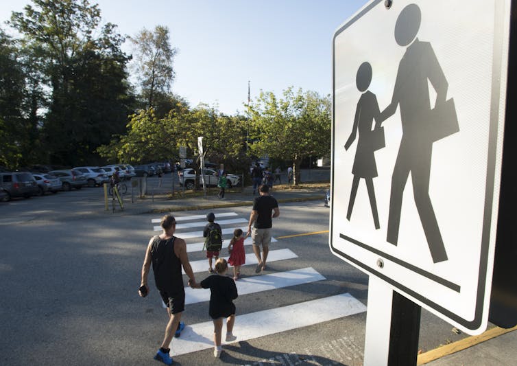 A parent and child seen crossing a crosswalk to go to school.