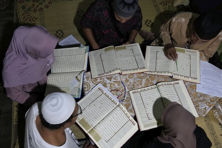 Trans women, some wearing hijabs, sit around a table reading from copies of the Quran.