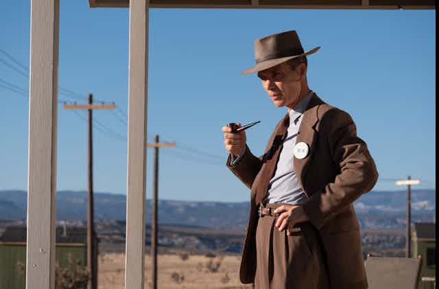 Image from the movie 'Oppenheimer' of the title character standing outdoors with a pipe