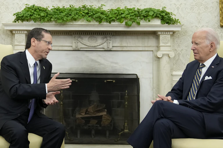 Two men in suits sit in a room talking.