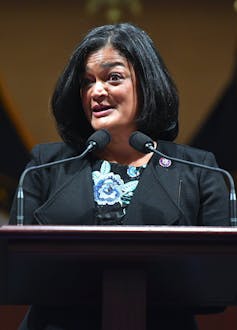 A woman with black hair wearing a dark suit speaking into a microphone