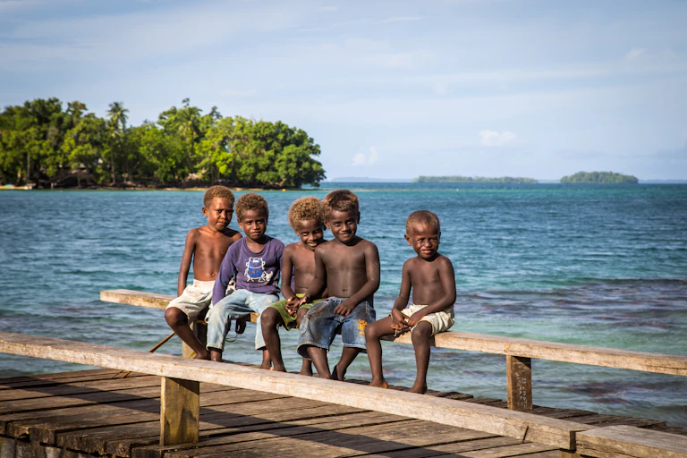 Group of children sitting on a wooden pier in the Solomon Islands, with their backs to the sea.
