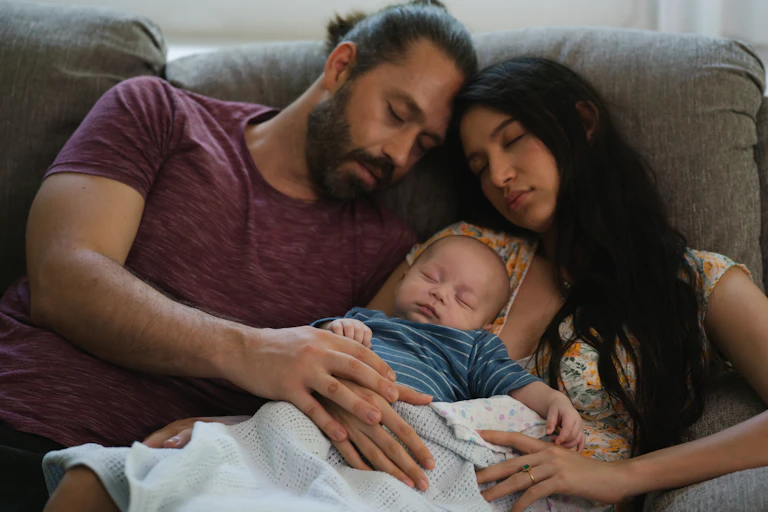 Parents and a newborn, all asleep on a sofa