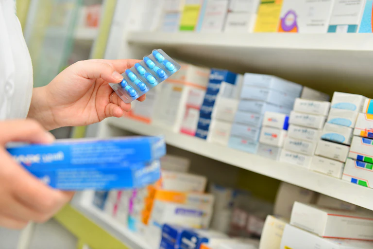 person holds tablet blister pack in front of pharmacy shelves