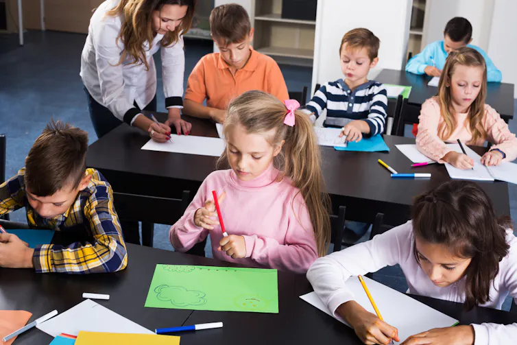 Enfants assis à leur table en classe et dessinant avec les conseils de leur enseignante