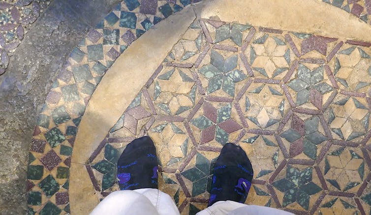 A pair of besocked feet on a floor mosaic.