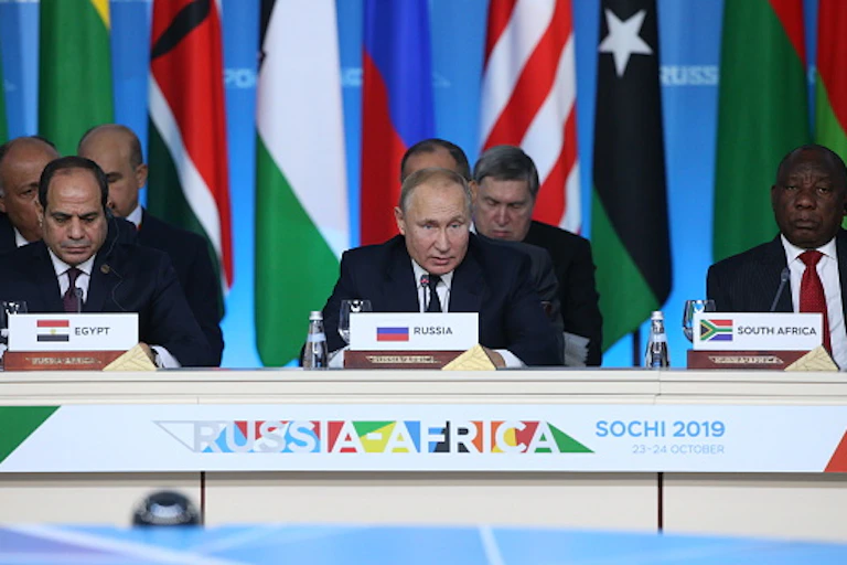 Three male presidents wearing ties address a press conference behind a desk with the sign Russia-Africa, Sochi 2019.