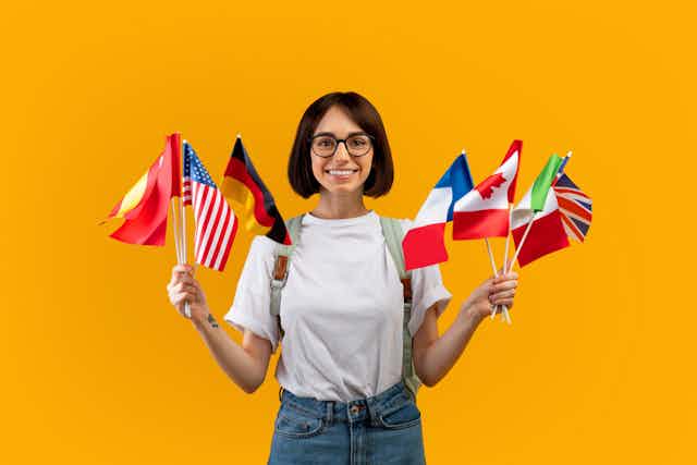 Una mujer mira a cámara y sujeta banderas de diferentes países.