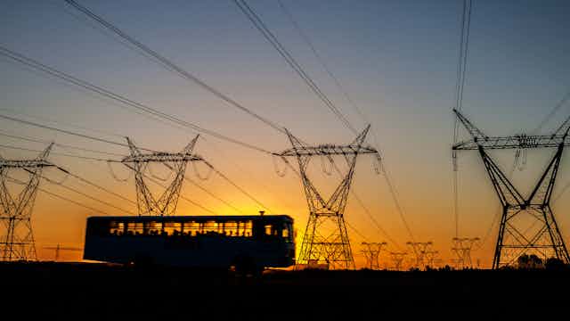 Bus with passengers driving by power lines in South Africa at sunset.