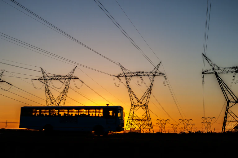 Bus with passengers driving by power lines in South Africa at sunset.