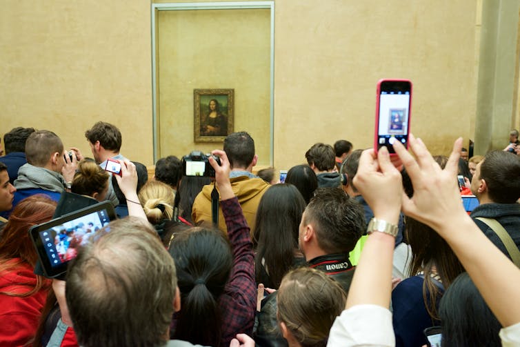 Crowds of tourists clamoring to take a photo of the Mona Lisa at the Louvre museum in Paris.