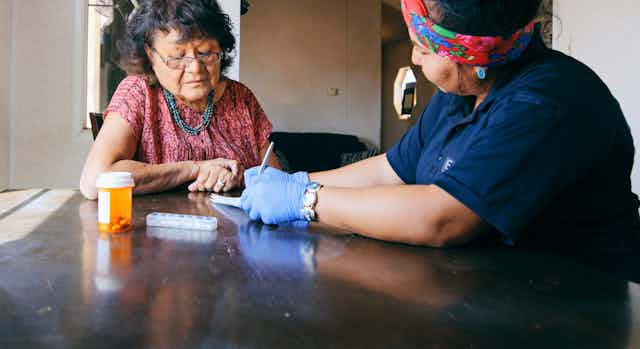 A nurse visiting an older patient at home assists with medication.