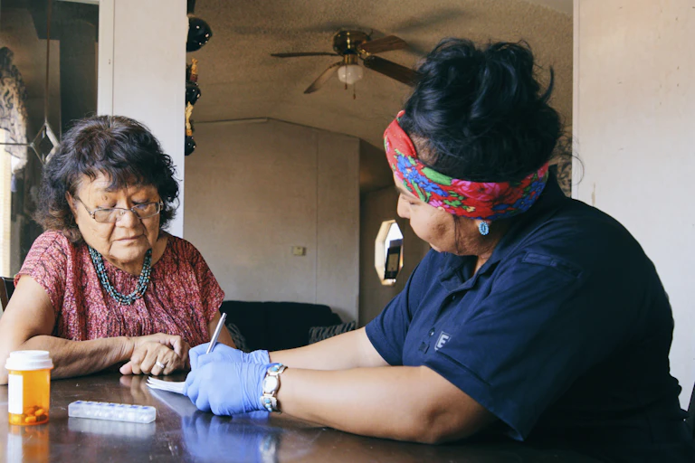 A nurse visiting an older patient at home assists with medication.