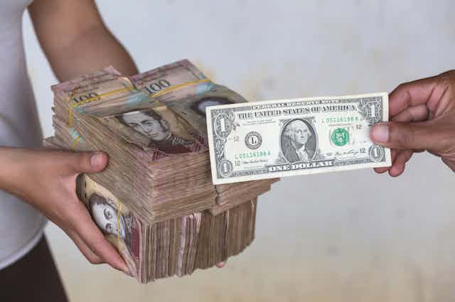 Unas manos ofrecen miles de bolívares a cambio de un dólar.
