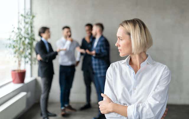 A women looks at a group of male colleagues duscussing together.
