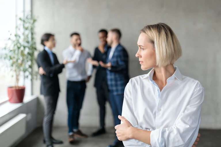A women looks at a group of male colleagues duscussing together.