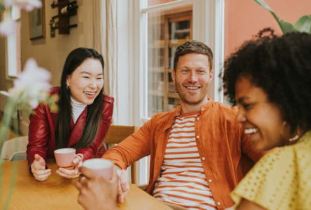 three people with big smiles chat at table with coffee cups
